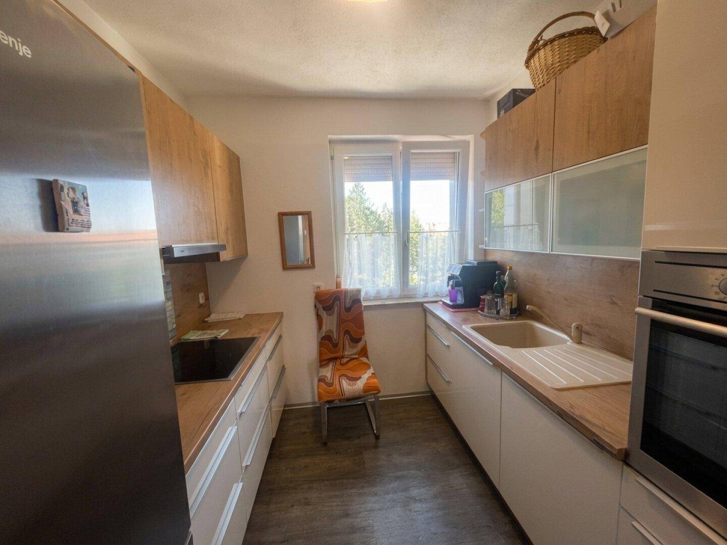 Funktionale Küche mit Holz- und weißen Schränken, Spüle, Backofen und Kühlschrank, mit Fenster.