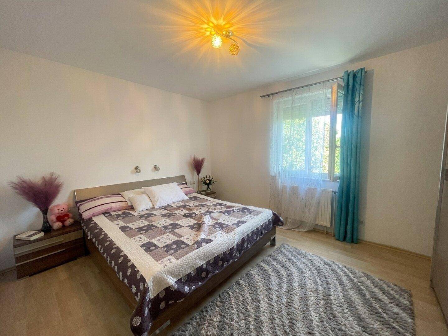 Geräumiges Schlafzimmer mit Doppelbett, Teppich und Fenster mit blauen Vorhängen, hell und einladend.