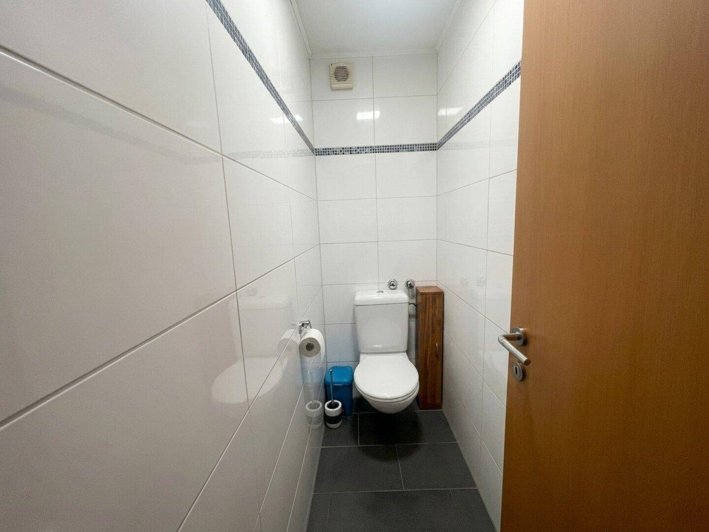 Kleines, hell gefliestes WC mit Toilette und dunklem Boden, sauber und funktional.