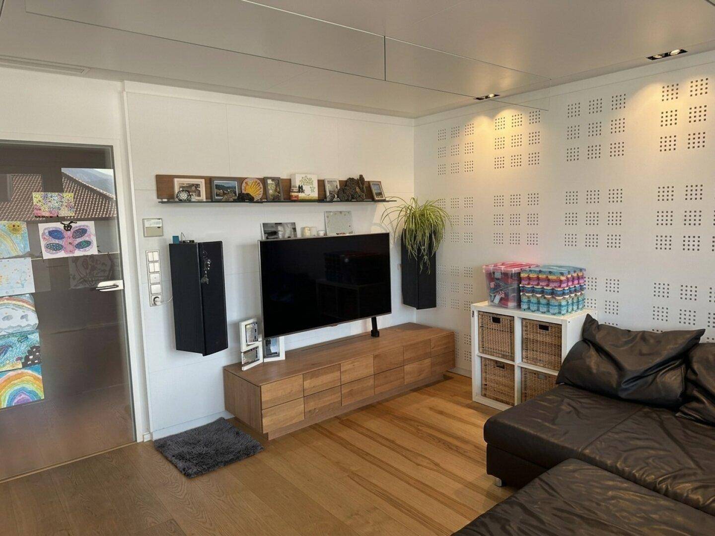 Gemütliches Wohnzimmer mit Fernseher, Holzmöbeln und dunklem Ledersofa.