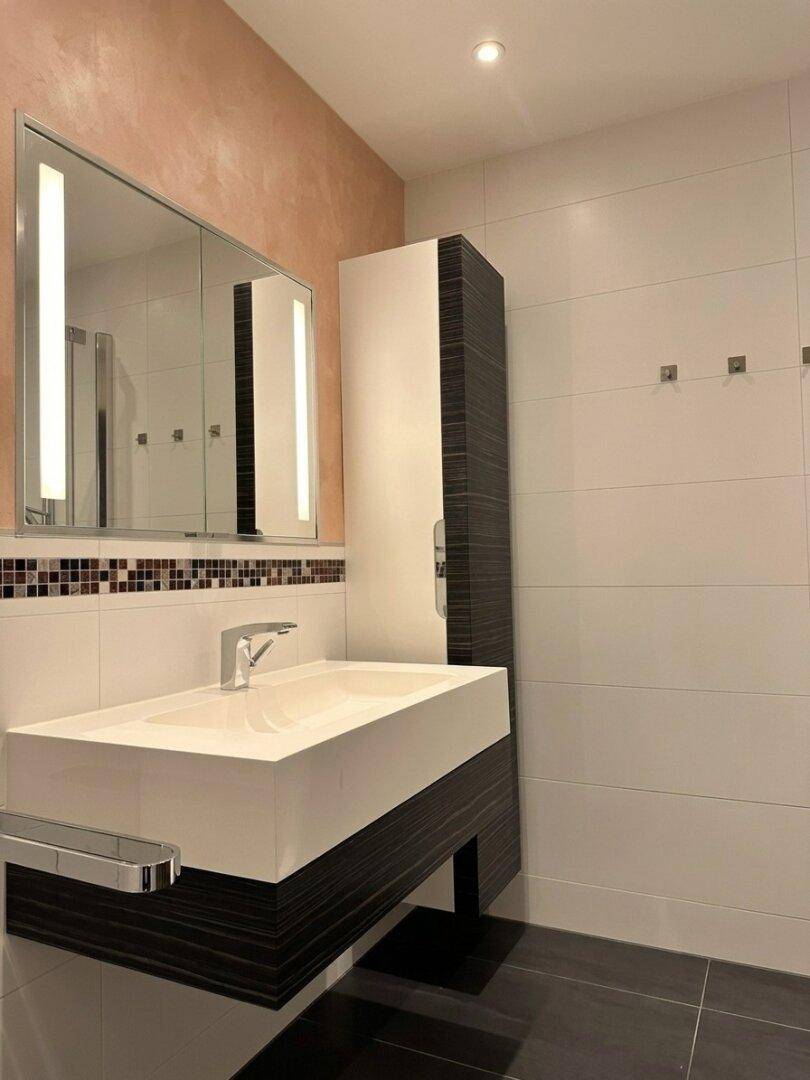 Modernes Badezimmer mit schwebendem Waschbecken, Spiegelschrank und eleganten Fliesen.
