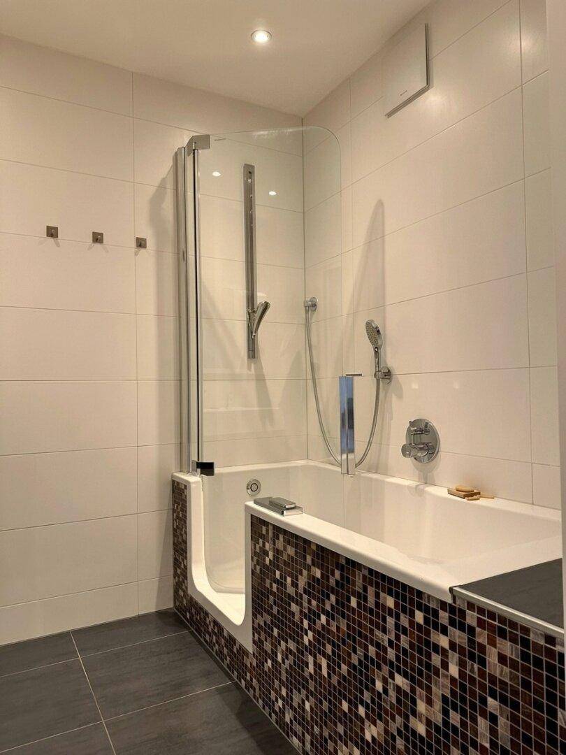 Badezimmer mit Badewanne, Duschabtrennung aus Glas und dekorativen Mosaikfliesen.