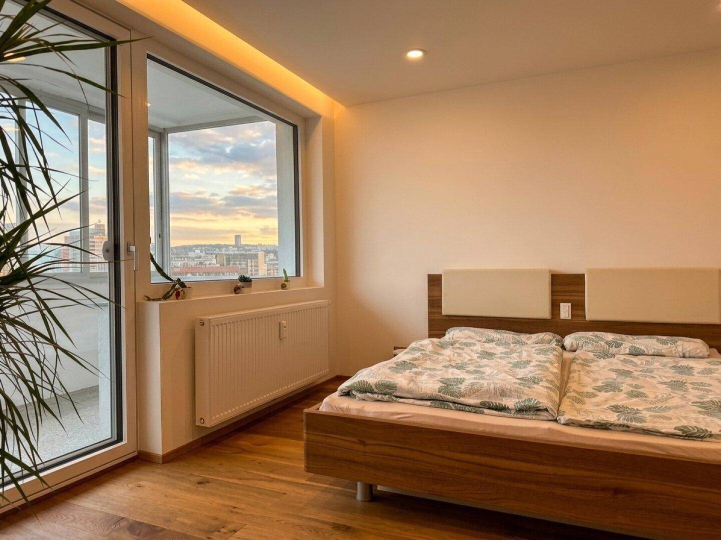 Schlafzimmer mit Doppelbett, großen Fenstern und Zugang zu einem Balkon.