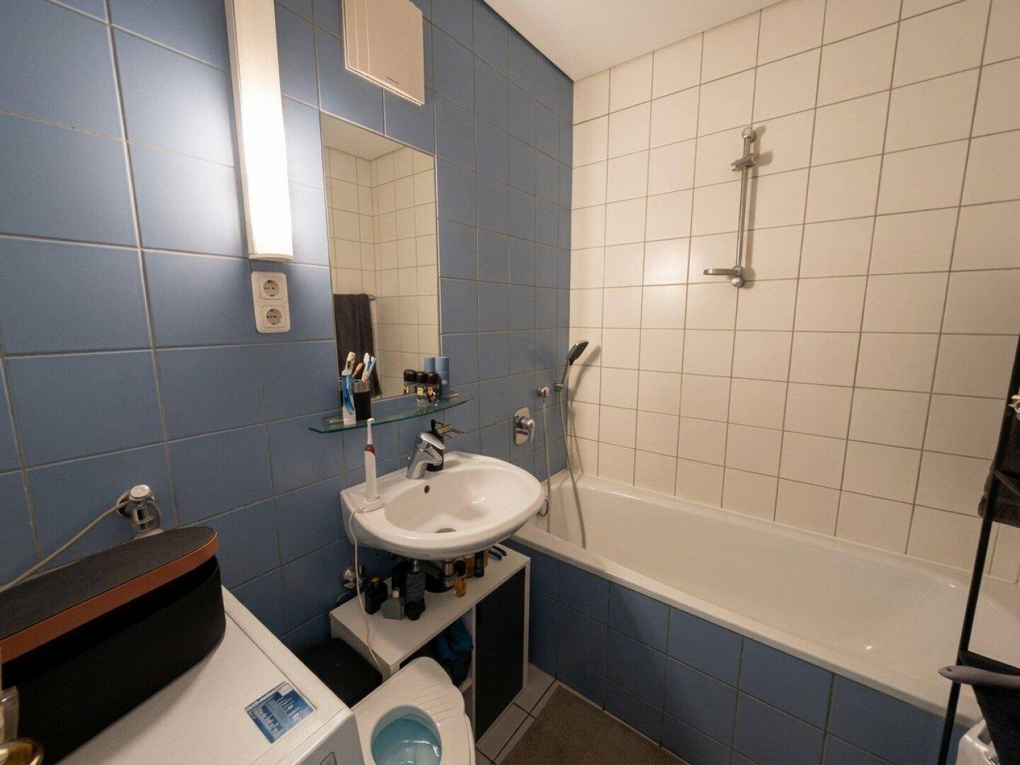 Badezimmer mit blauen und weißen Fliesen, einer Badewanne mit Duschfunktion und einem Waschbecken.