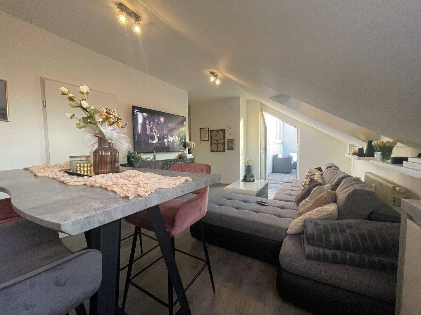 Geräumiges Wohnzimmer mit großem Ecksofa, Fernseher und Blick auf den Essbereich unter der Dachschräge.
