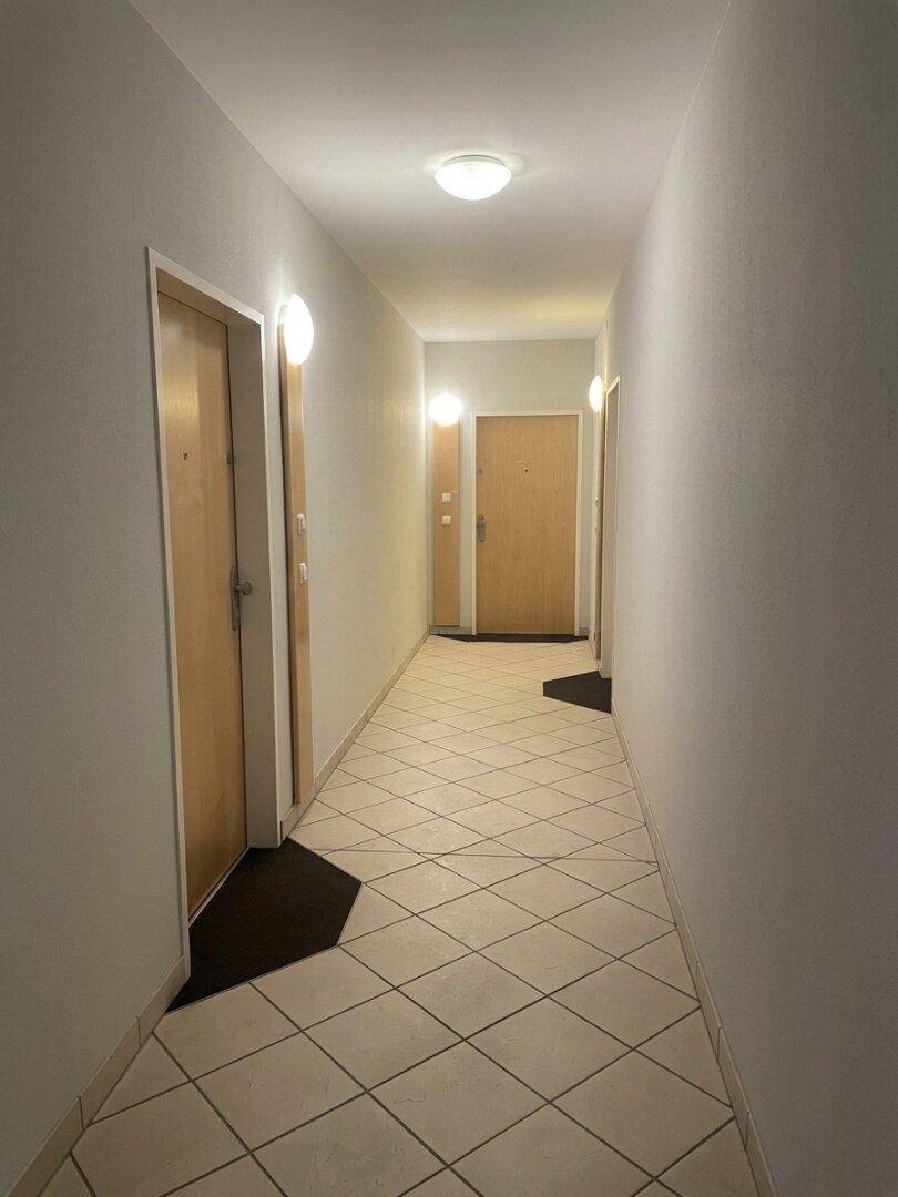 Langer, heller Flur mit hellen Fliesen und mehreren Türen, die zu den Zimmern führen.
