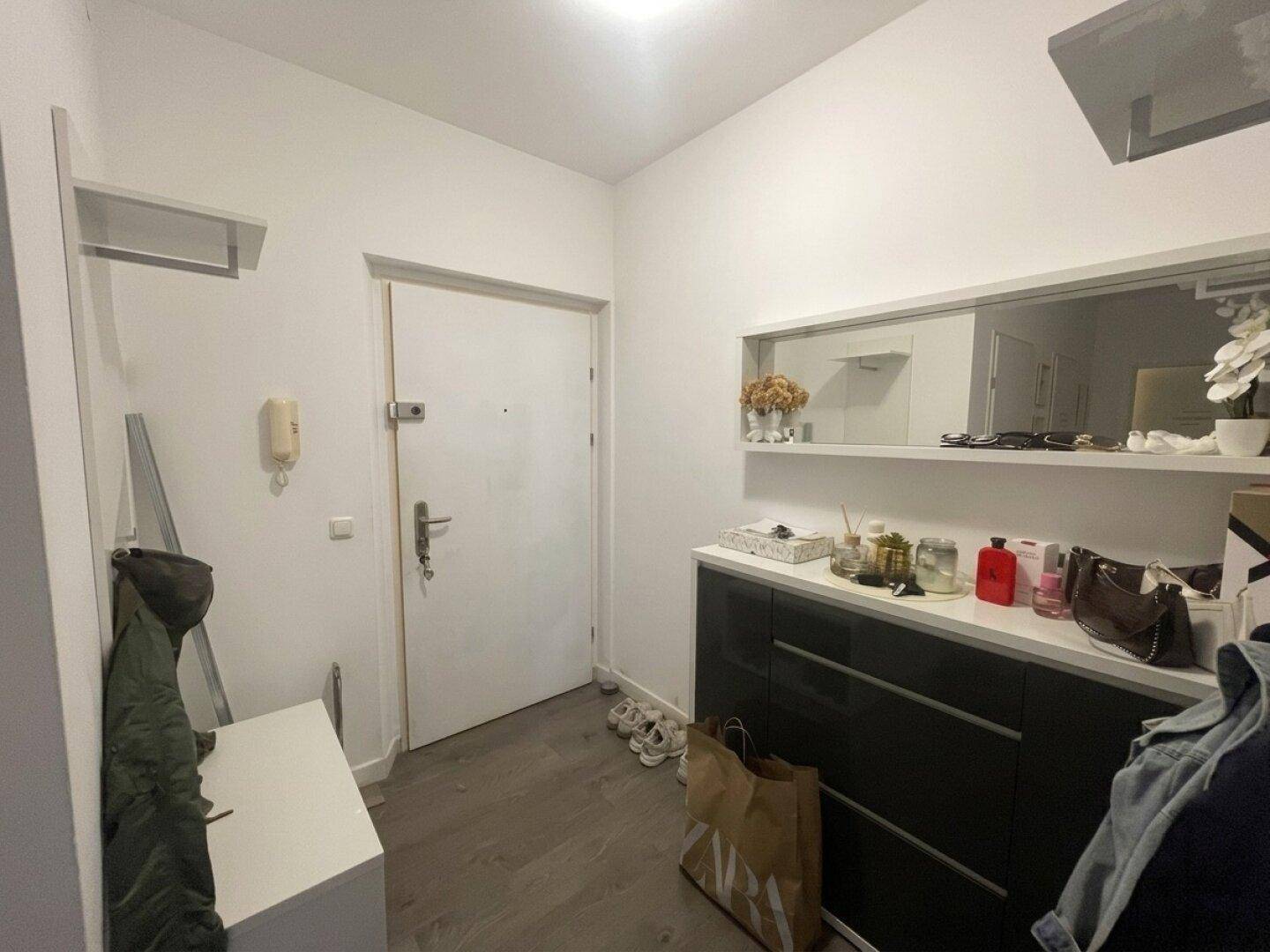 Heller Eingangsbereich mit weißer Tür, dunklem Sideboard, Spiegel und Garderobe.