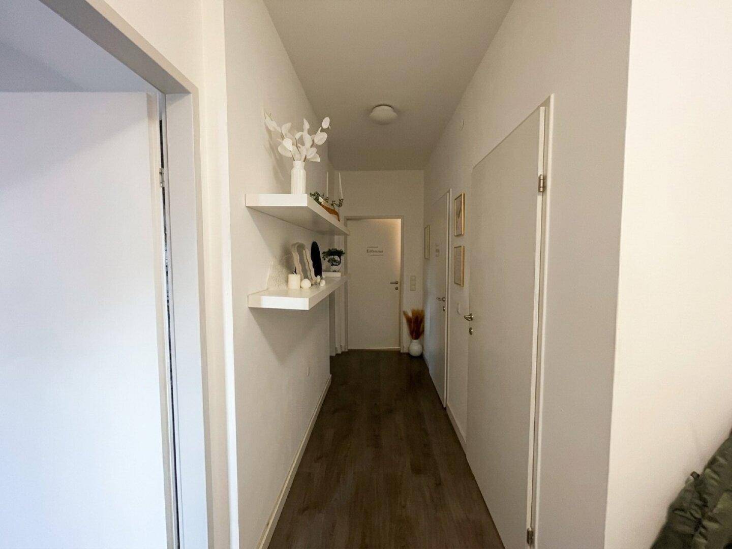 Heller Flur mit weißen Wänden, schwebenden Regalen und einem modernen Laminatboden.