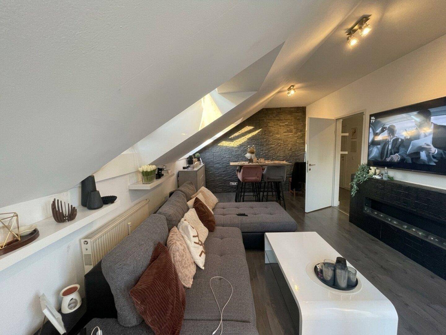 Geräumiges Wohnzimmer mit großem Ecksofa, Fernseher und Blick auf den Essbereich unter der Dachschräge.