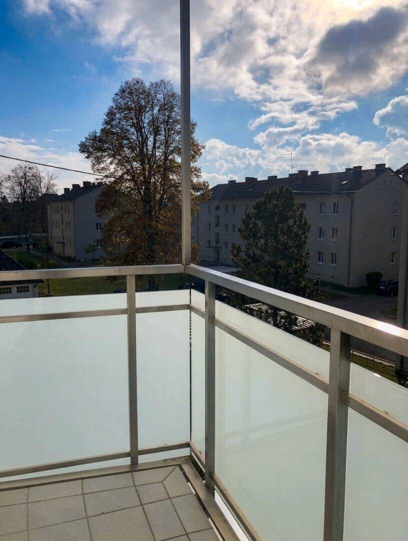 Balkon mit Glasgeländer und Ausblick auf die umliegenden Wohngebäude und Bäume.