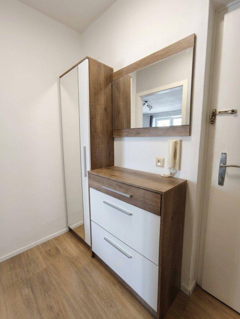 Heller Flur mit Garderobe, Spiegel und Kommode in Holz-Weiß-Optik.