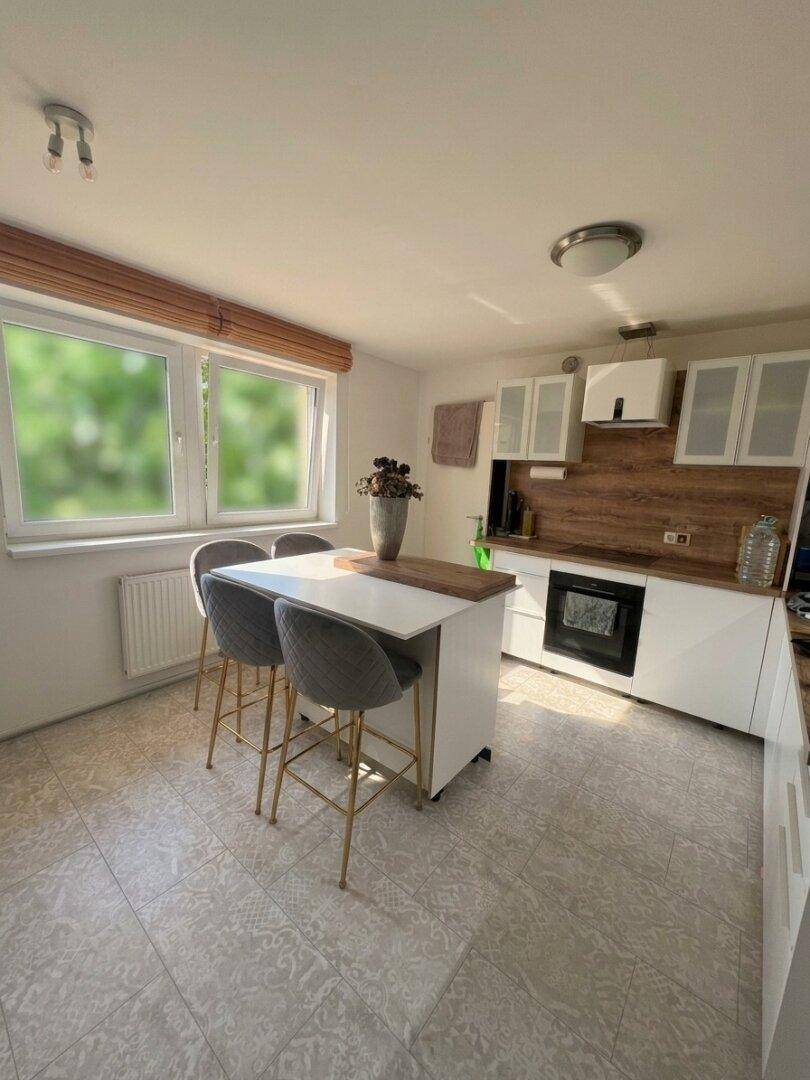 Helle Küche mit Kücheninsel, Frühstücksbar und Fenster mit Blick ins Grüne.