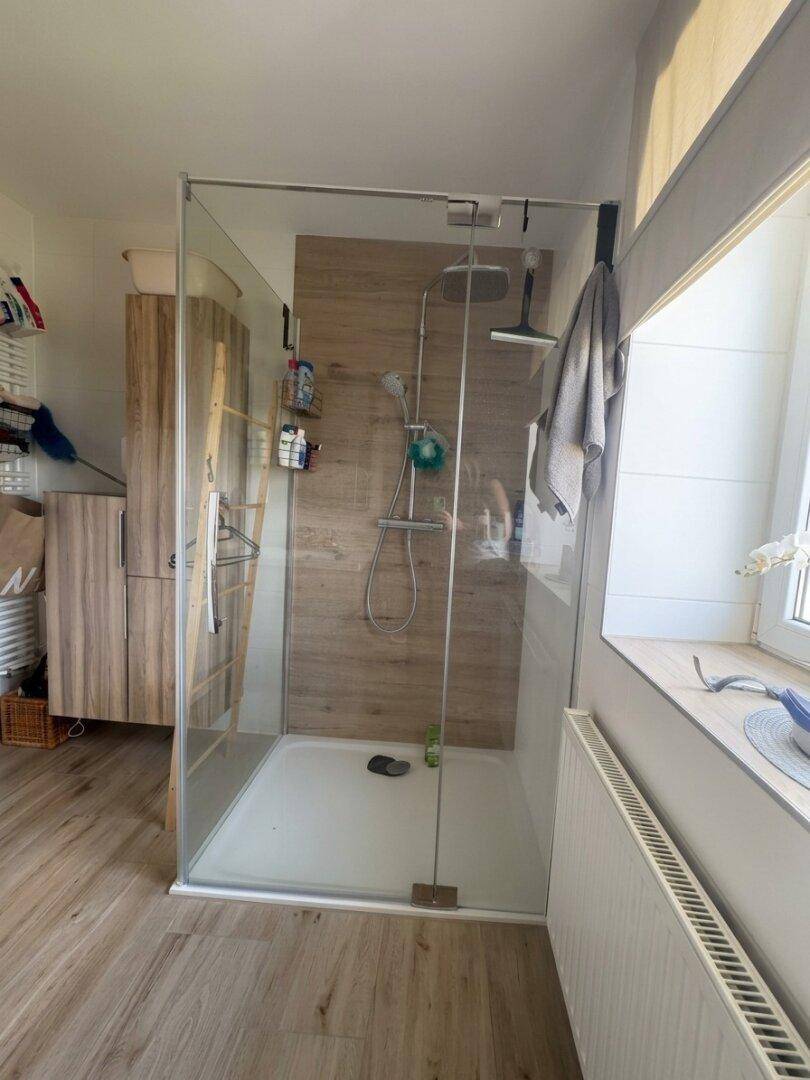Modernes Badezimmer mit begehbarer Glasdusche und Holzoptik-Fliesen an der Wand.