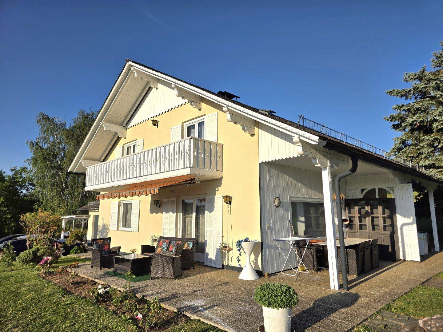 Seitliche Ansicht des Hauses mit überdachter Terrasse und Gartenmöbeln, umgeben von Grün.