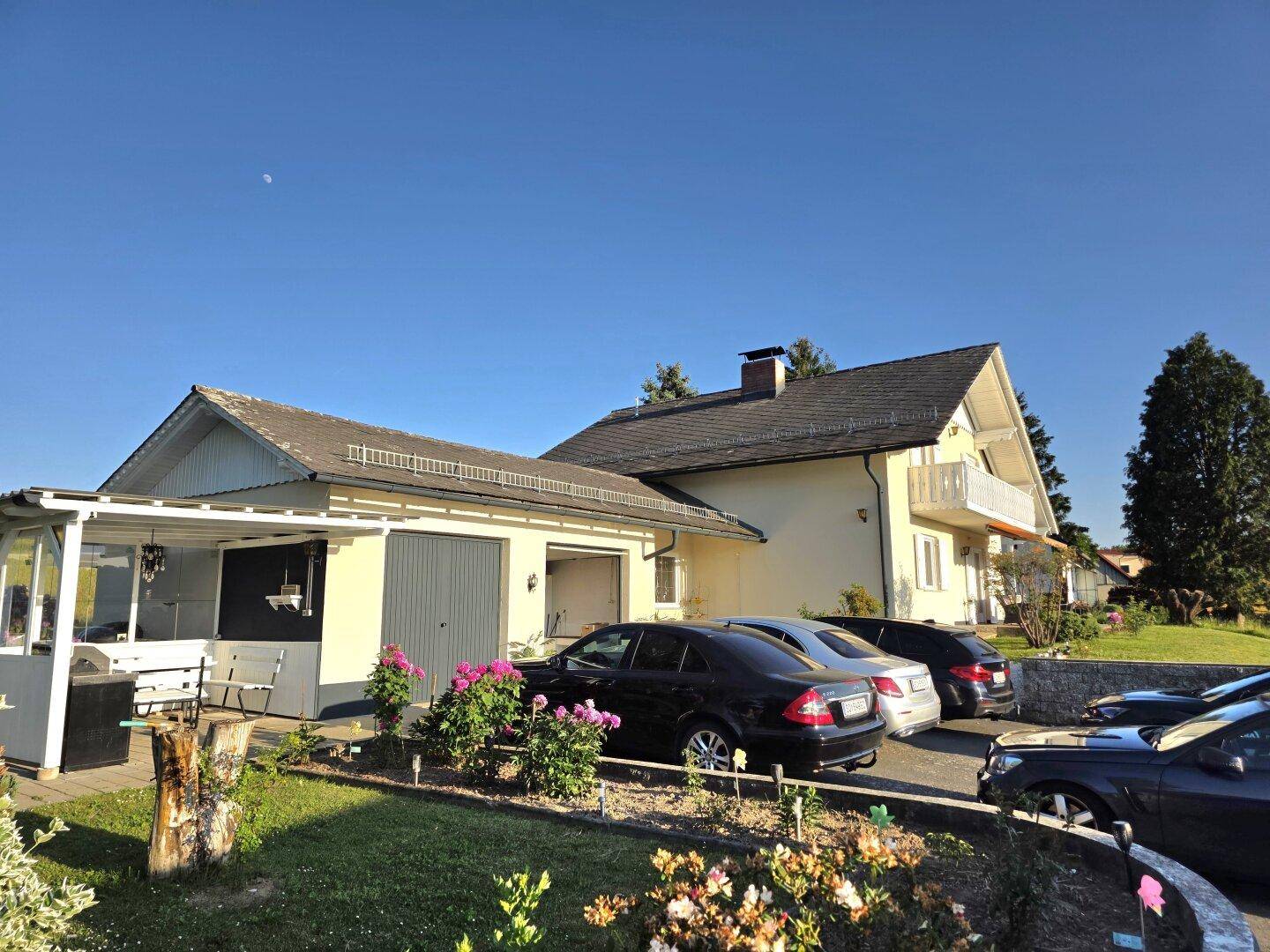 Ansicht des Hauses mit Garage, Carport und mehreren geparkten Autos im Vorgartenbereich.
