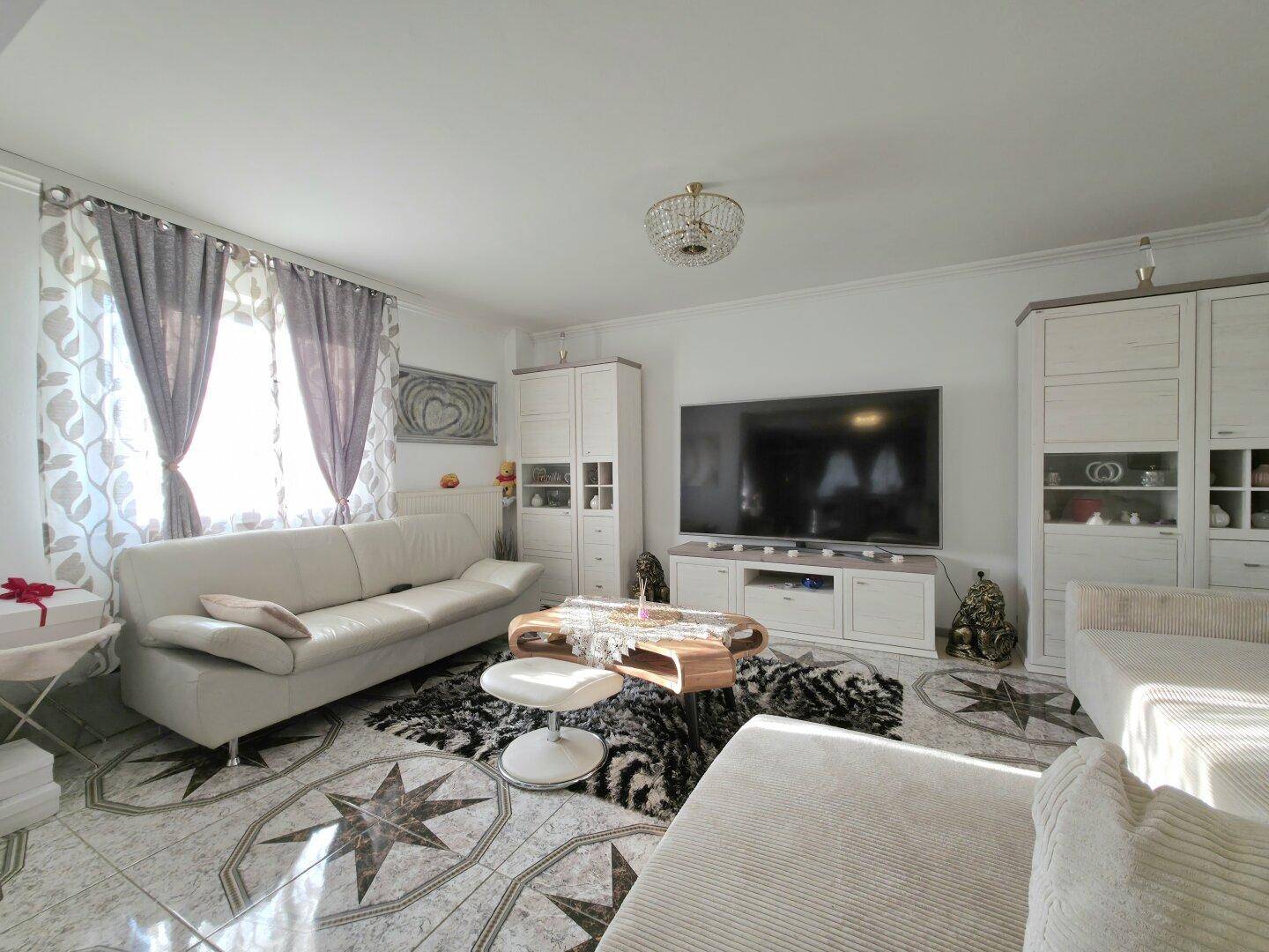 Helles Wohnzimmer mit bequemen Sofas, großem Fernseher und auffälligem Fliesenbodenmuster.