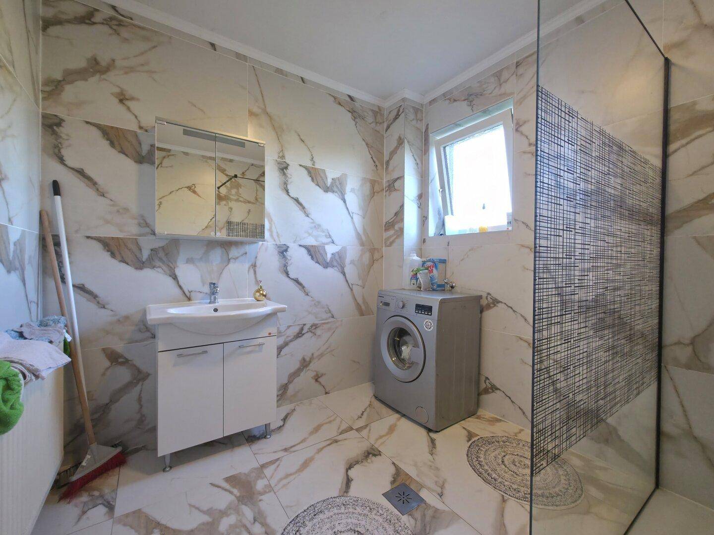Modernes Badezimmer mit Marmorfliesen, Waschbeckenunterschrank und einer Duschkabine.