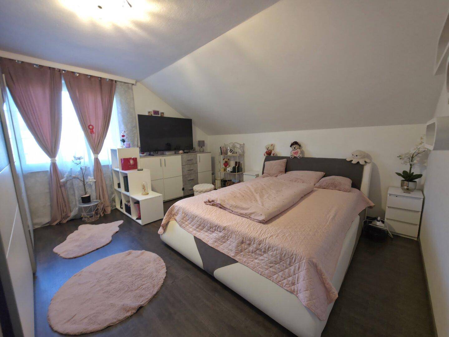 Gemütliches Schlafzimmer im Dachgeschoss mit schrägen Wänden, großem Bett und dunklem Boden.