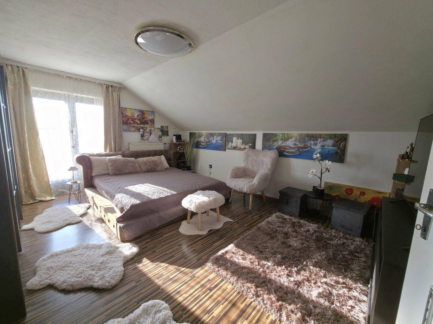 Geräumiges Schlafzimmer im Dachgeschoss mit Holzboden, großem Bett und flauschigen Teppichen.
