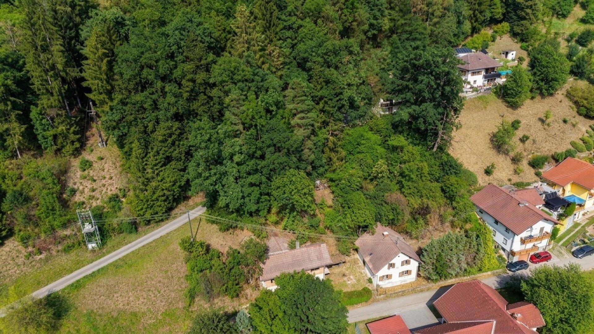 Blick von oben auf bewaldete Hügel und einige Häuser in einer ländlichen Umgebung.