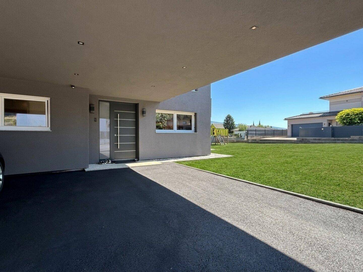 Moderner Eingangsbereich mit Carport und gepflegtem Vorgarten unter blauem Himmel.