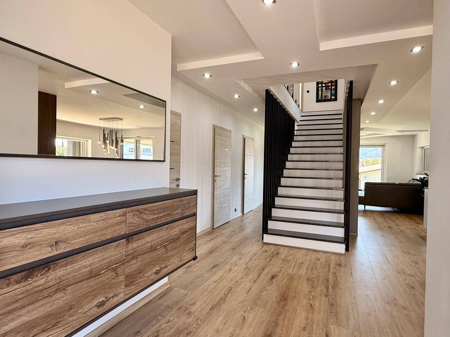 Heller Flur mit Holzoptikboden, moderner Kommode und offener Treppe zum Obergeschoss.