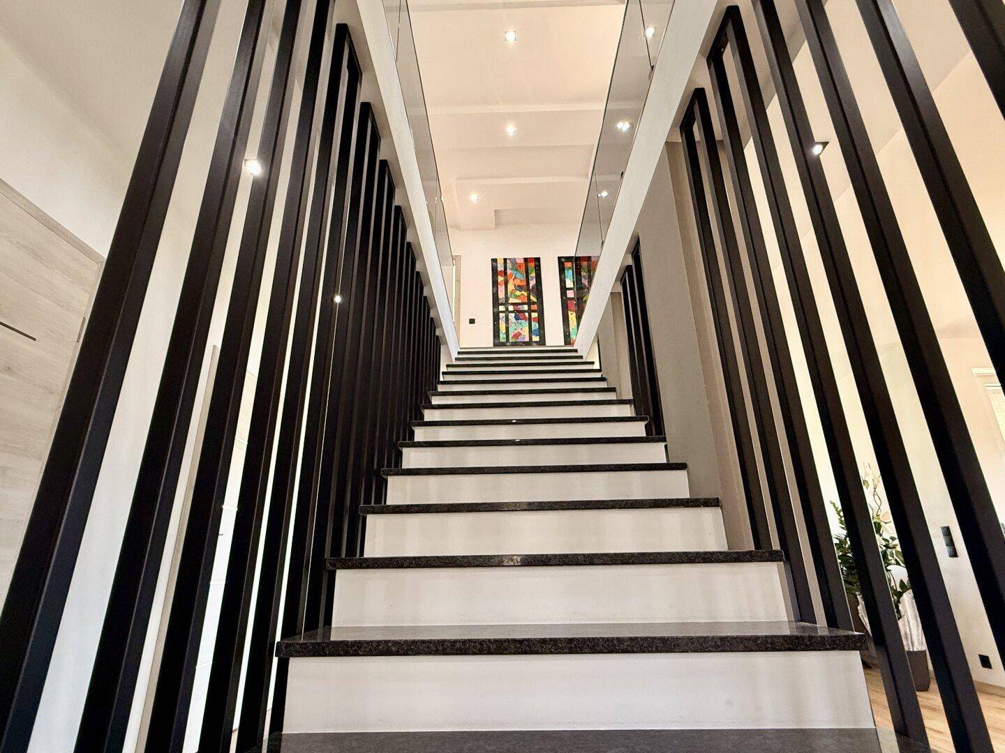 Moderne Treppe mit dunklen Stufen und vertikalen Geländerstäben, die zum Obergeschoss führt.