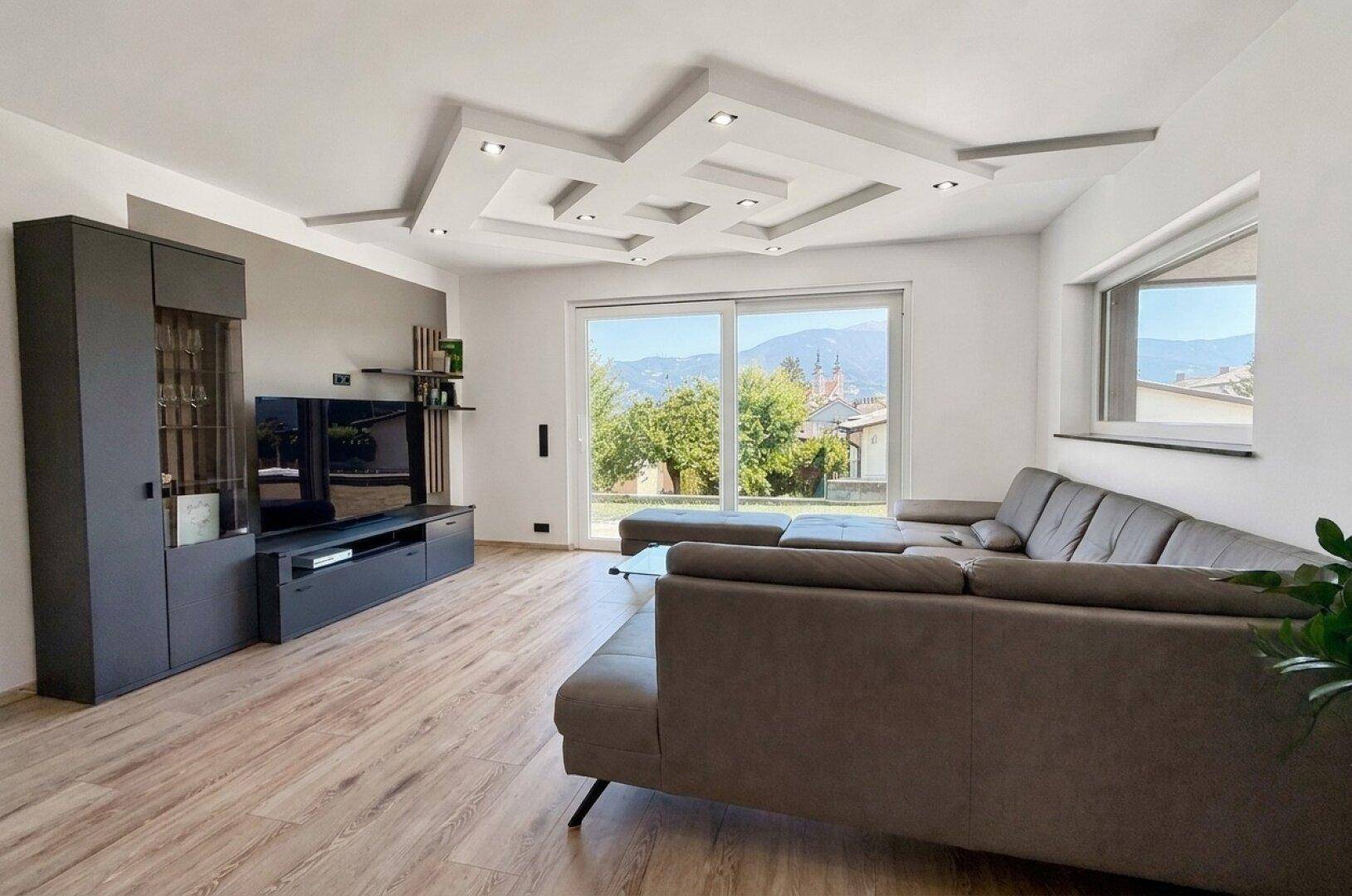 Helles Wohnzimmer mit großzügiger Couch, Medienwand und Zugang zur Terrasse mit Bergblick.