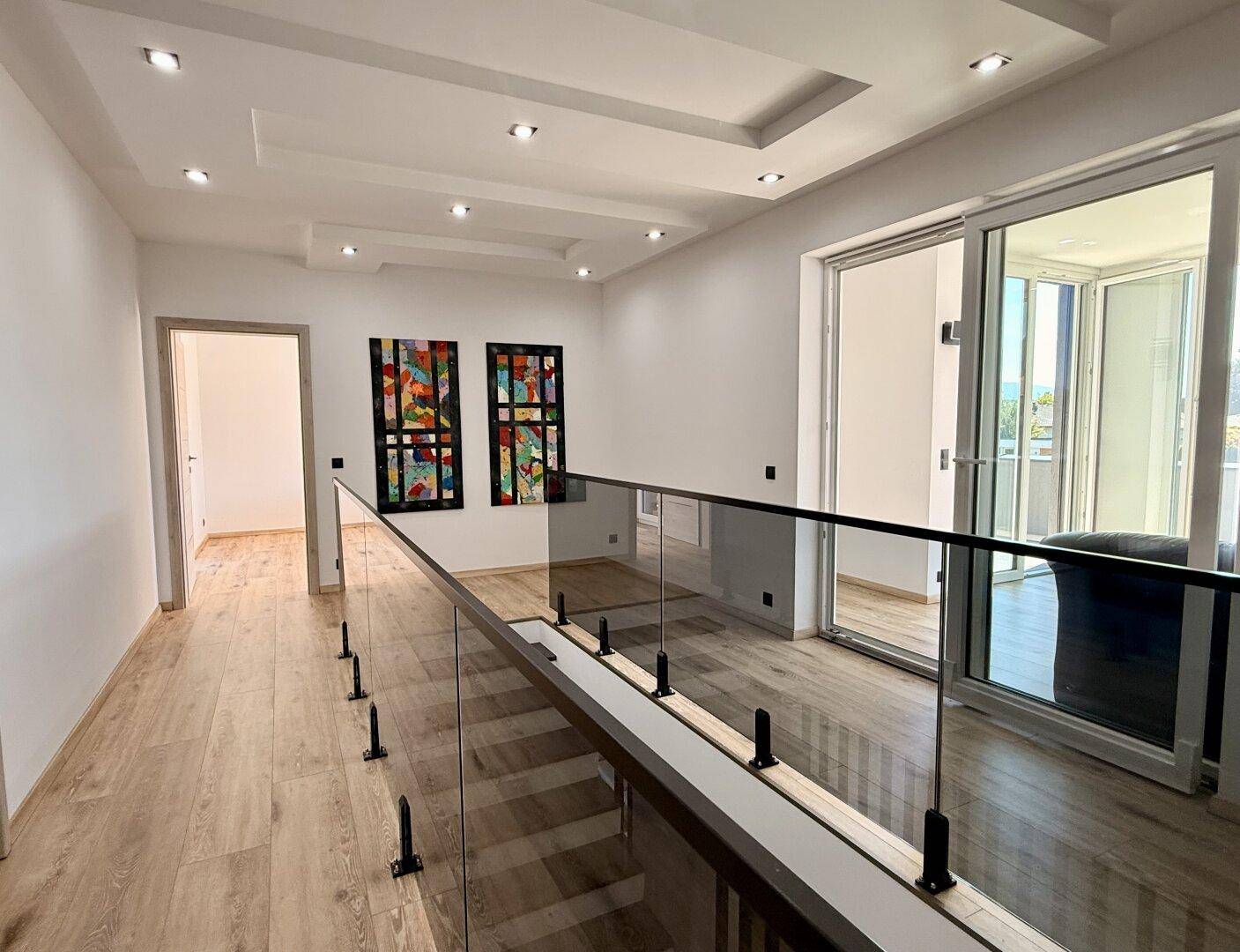 Heller Flur im Obergeschoss mit Glasgeländer und Zugang zu weiteren Räumen und Balkon.