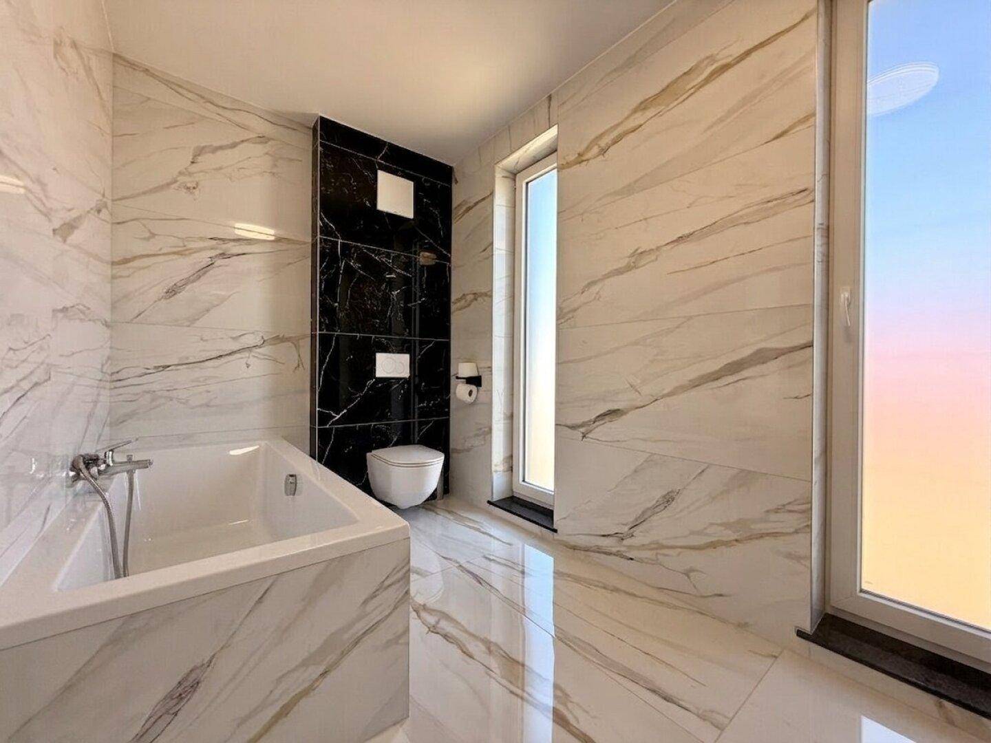 Modernes Badezimmer mit Badewanne, Wand-WC und großformatigen Marmorfliesen für luxuriöses Ambiente.