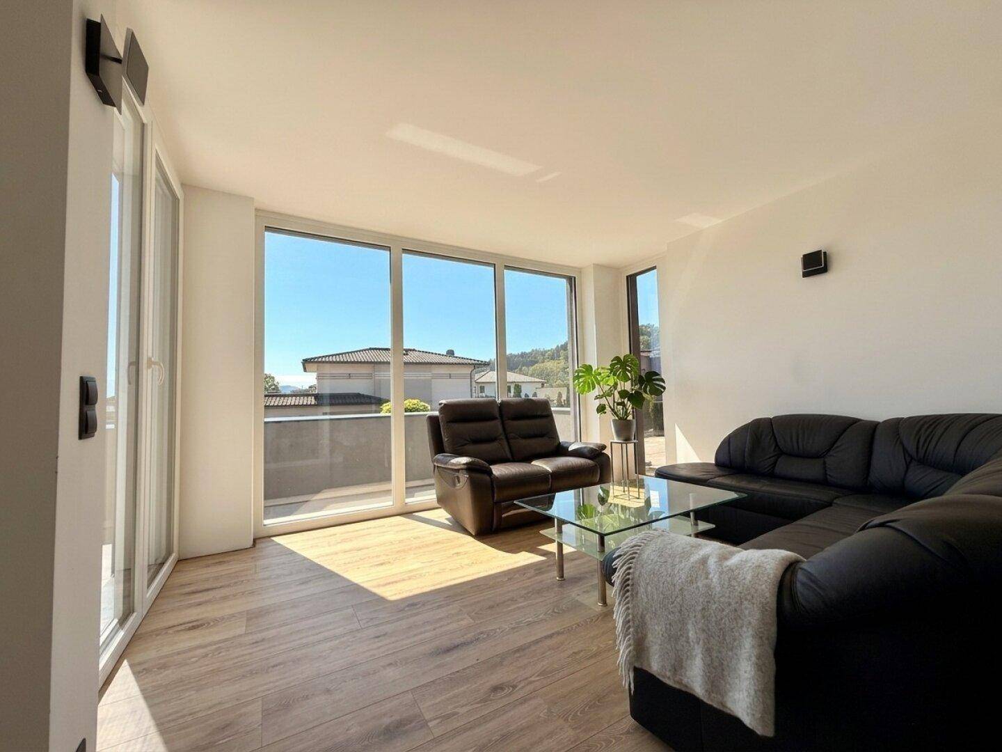 Lichtdurchflutetes Wohnzimmer mit großen Fenstern und Zugang zum Balkon, ideal zum Entspannen.