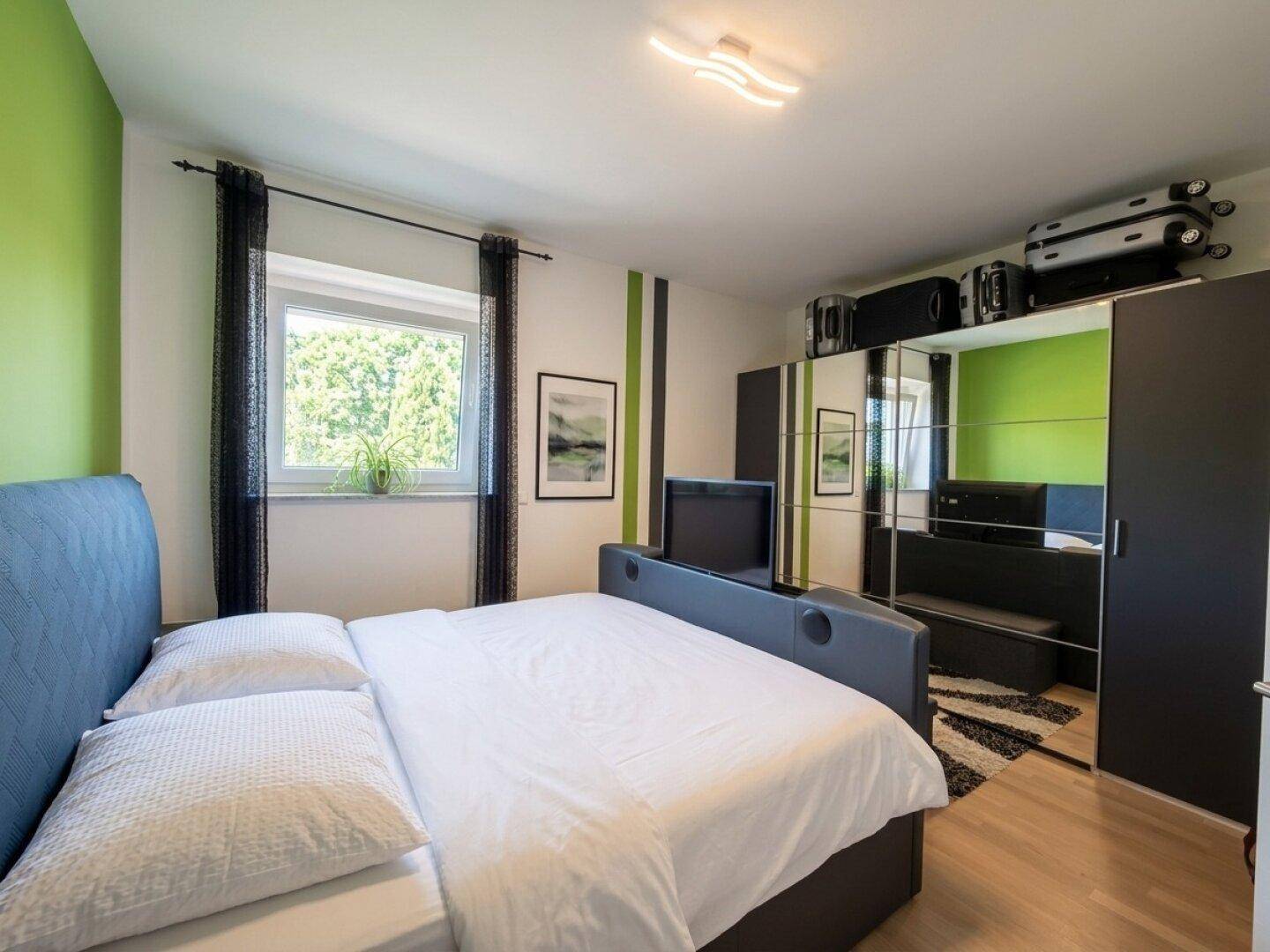 Helles Schlafzimmer mit Doppelbett, Spiegelschränken und grünen Akzentwänden.