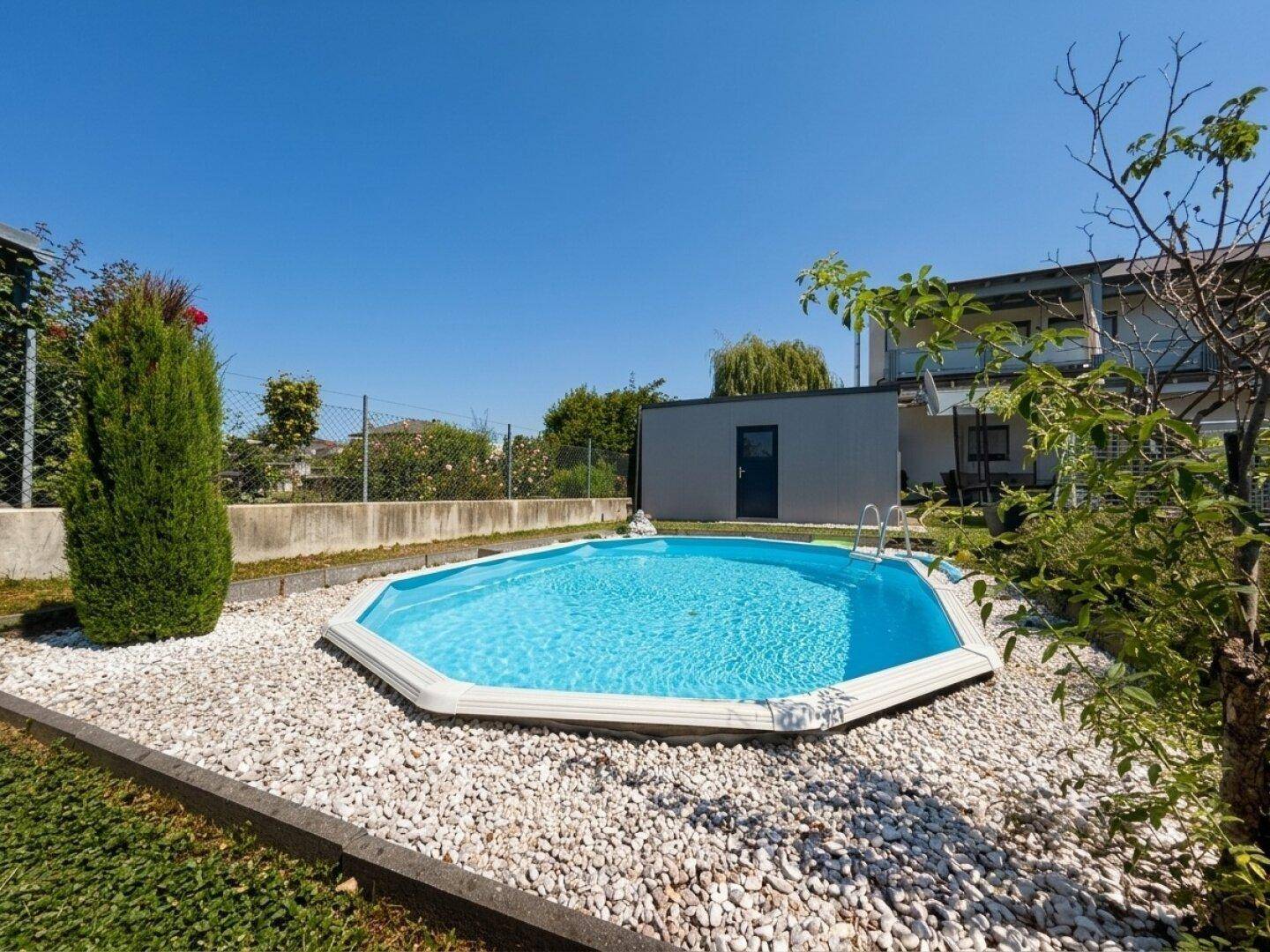 Attraktiver Swimmingpool im Garten, umgeben von weißen Zierkieseln und Grünflächen.