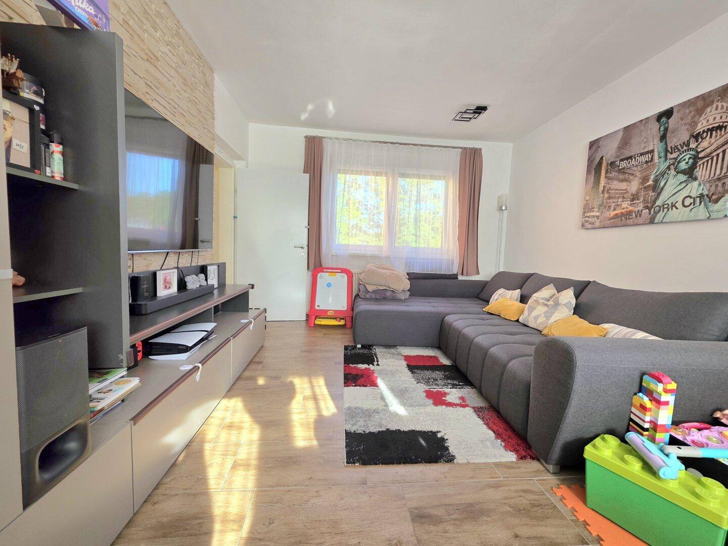 Gemütliches Wohnzimmer mit großem Ecksofa, Teppich und Blick auf den Außenbereich.