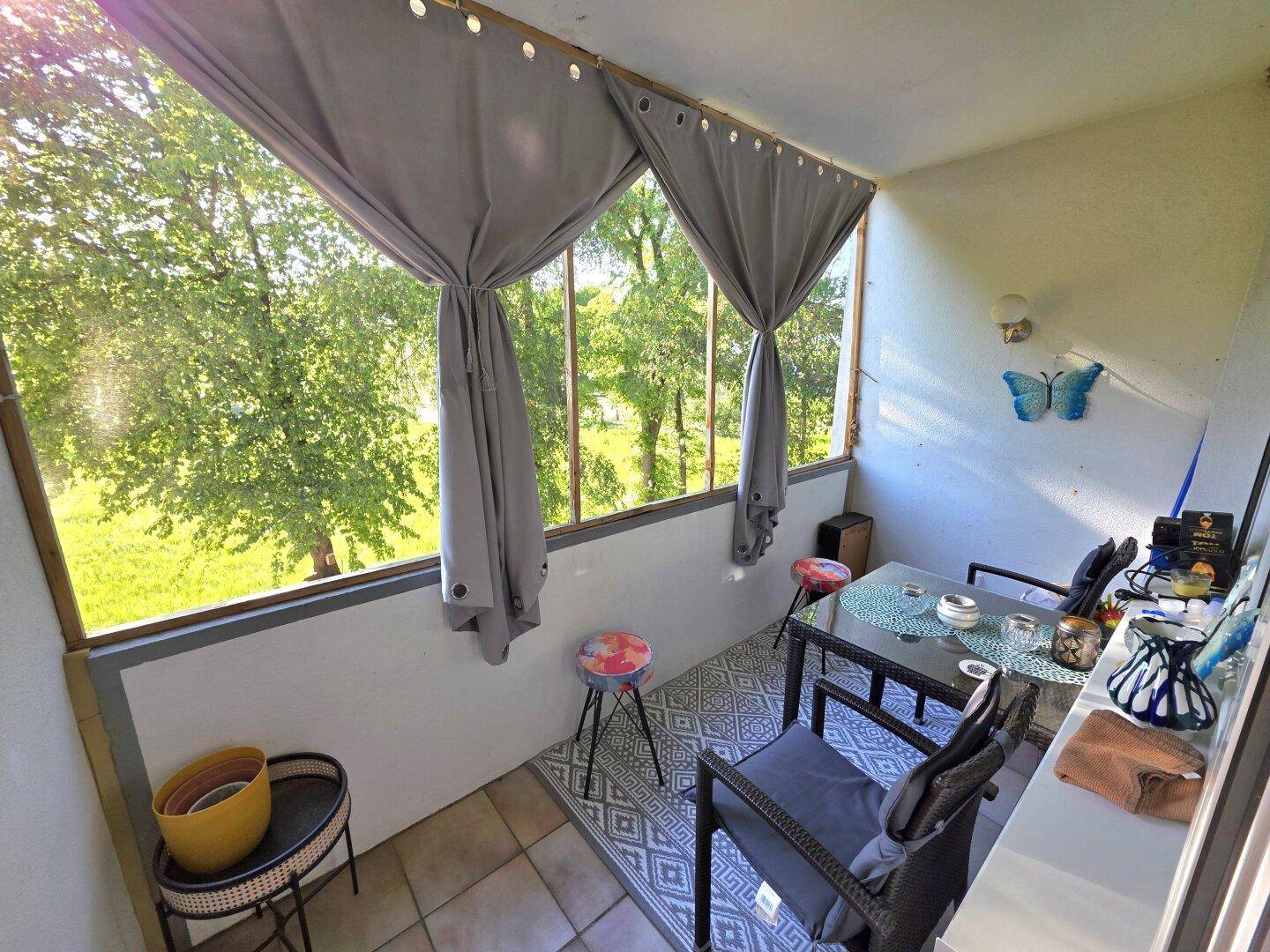 Gemütlicher Balkon mit Sitzgelegenheiten und Vorhängen, umgeben von viel Grün.