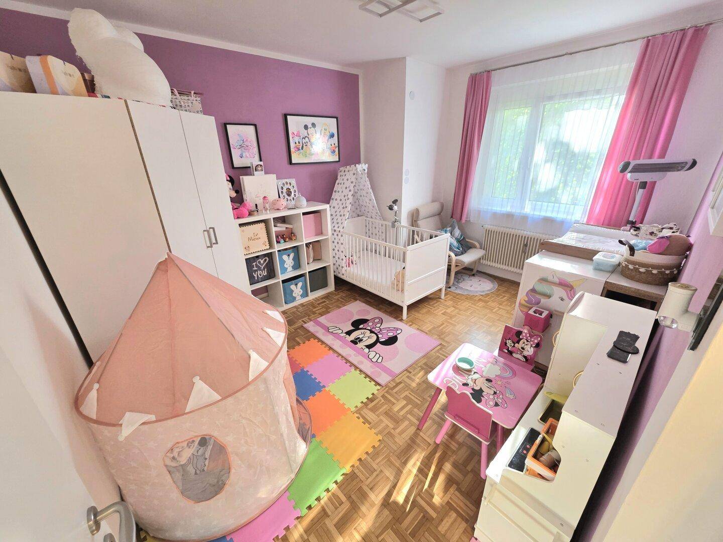 Farbenfrohes Kinderzimmer mit Babybett, Spielzelt und Minnie-Maus-Dekoration.