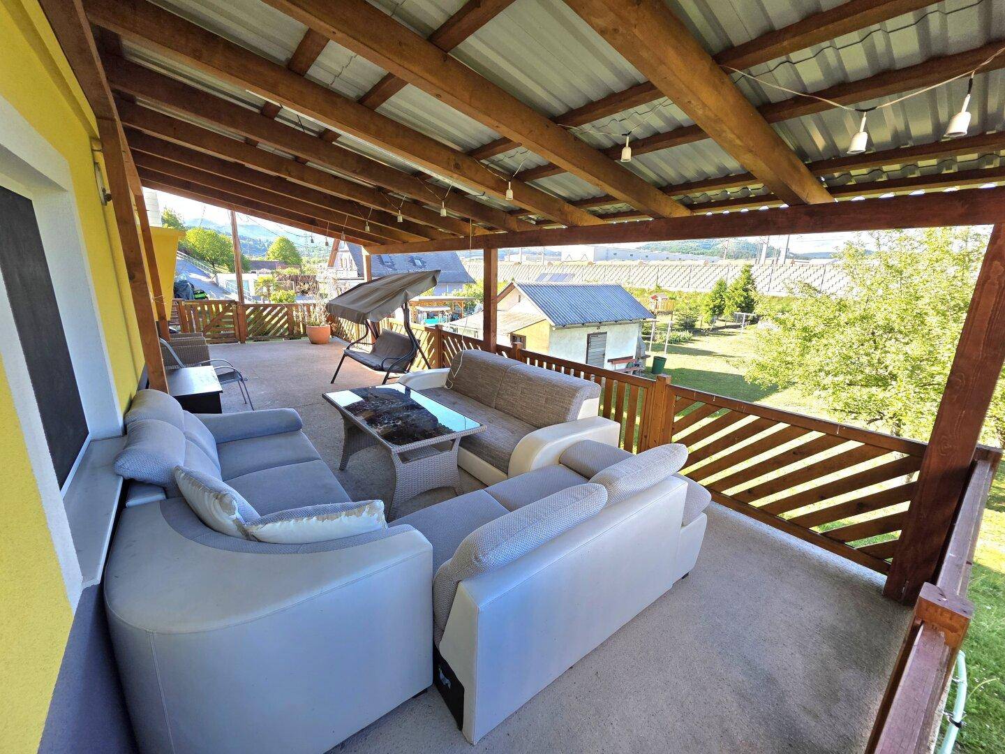 Geräumige überdachte Terrasse mit bequemen Loungemöbeln und Blick ins Grüne.