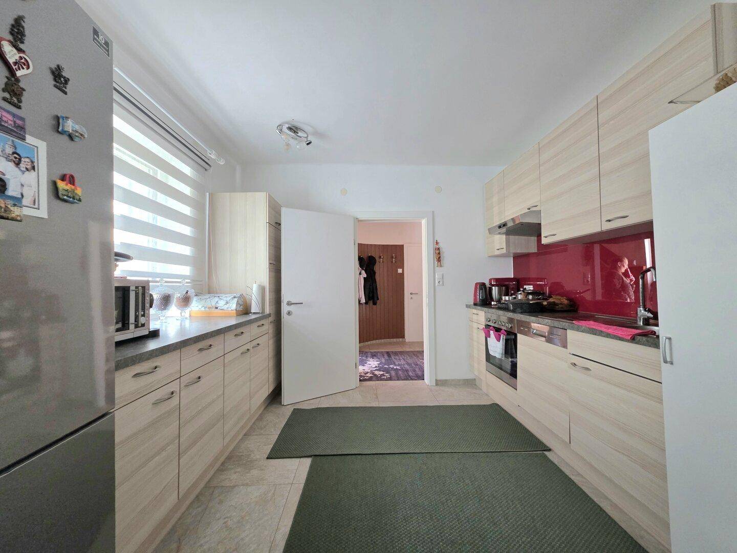 Moderne Küche mit hellen Holzfronten, roter Rückwand und Fliesenboden.