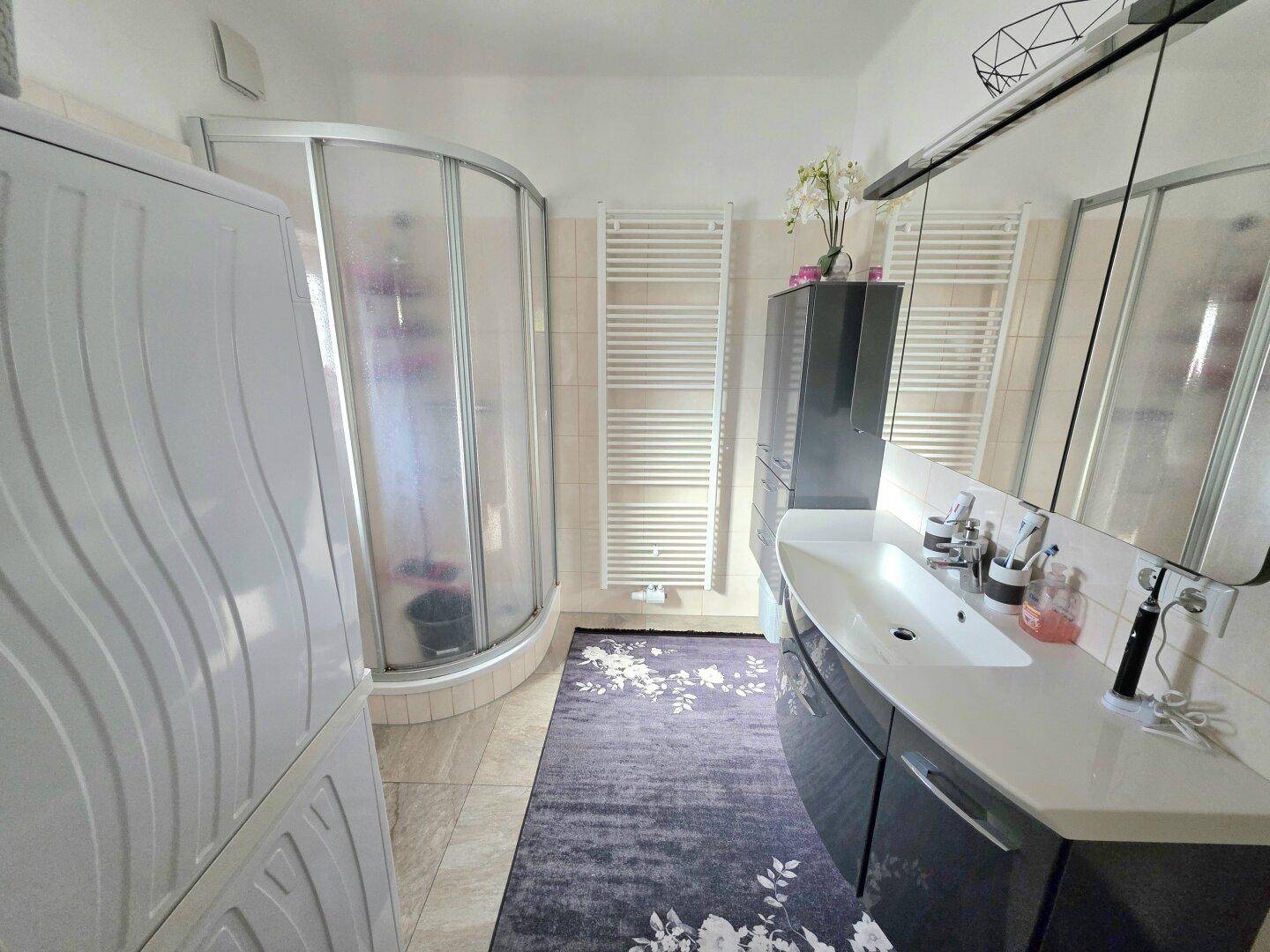 Helles Badezimmer mit Duschkabine, Einzelwaschbecken und beheiztem Handtuchhalter.
