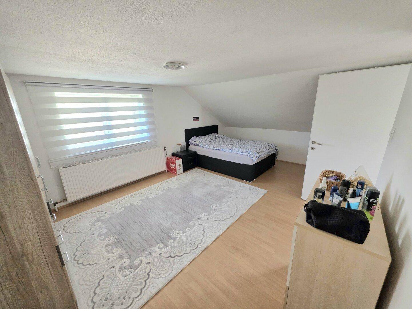 Schlafzimmer im Dachgeschoss mit Dachschräge, Einzelbett und hellem Laminatboden.