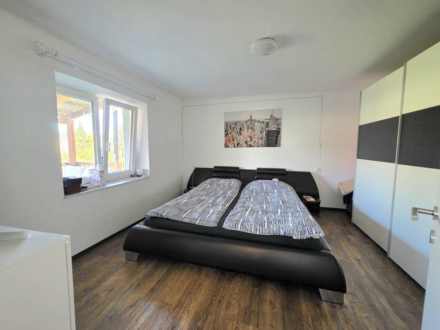 Schlafzimmer mit Doppelbett, Holzboden und Fenster mit Blick nach draußen.