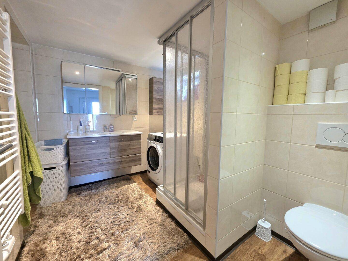 Badezimmer mit Duschkabine, Waschmaschine und WC, gefliest in hellen Tönen.