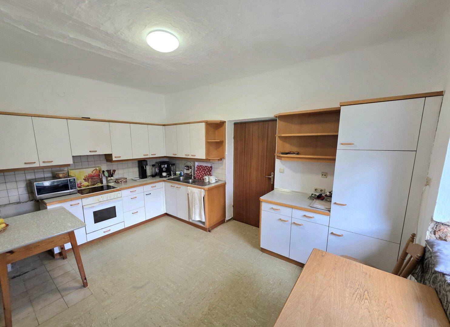 Geräumige Küche mit weißen Schränken, Holzdetails und älteren Einbaugeräten.