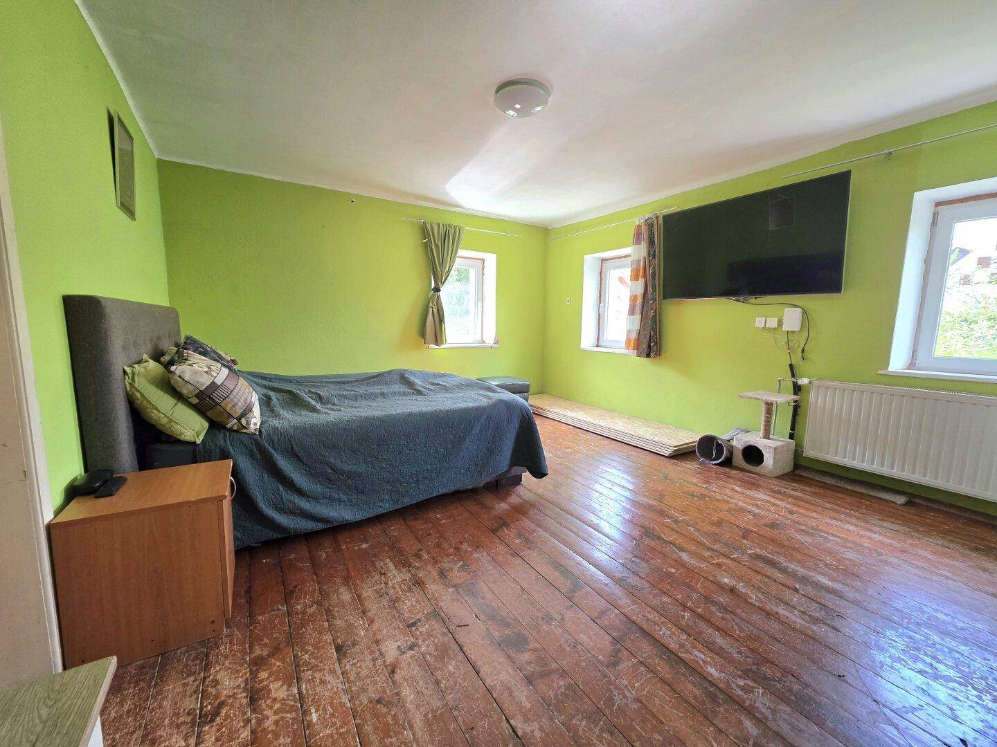 Schlafzimmer mit auffälligen grünen Wänden, Holzdielenboden und großem Flachbildfernseher.