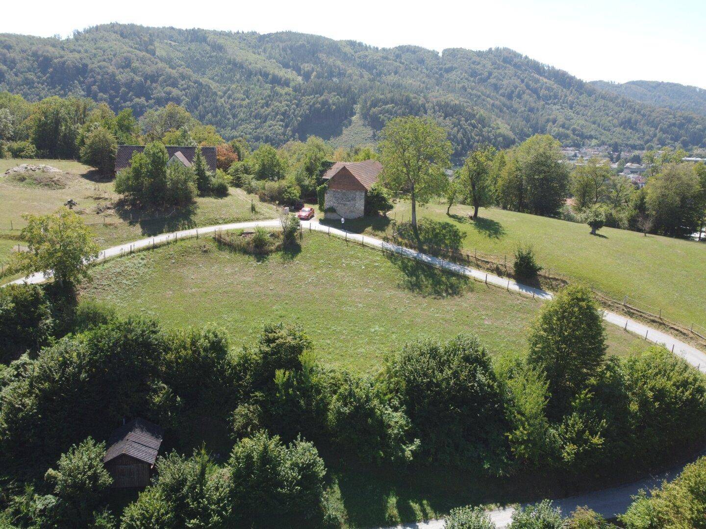 Panoramablick aus der Vogelperspektive auf eine hügelige Landschaft mit Wiesen und vereinzelten Häusern.