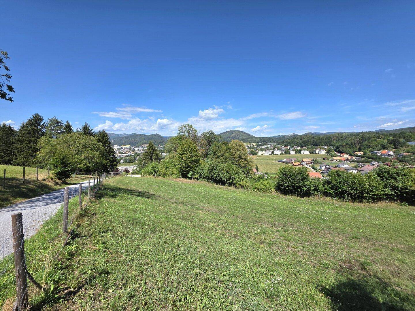 Grüne Landschaft mit einer Straße und einem Panoramablick auf eine Stadt und Berge in der Ferne.