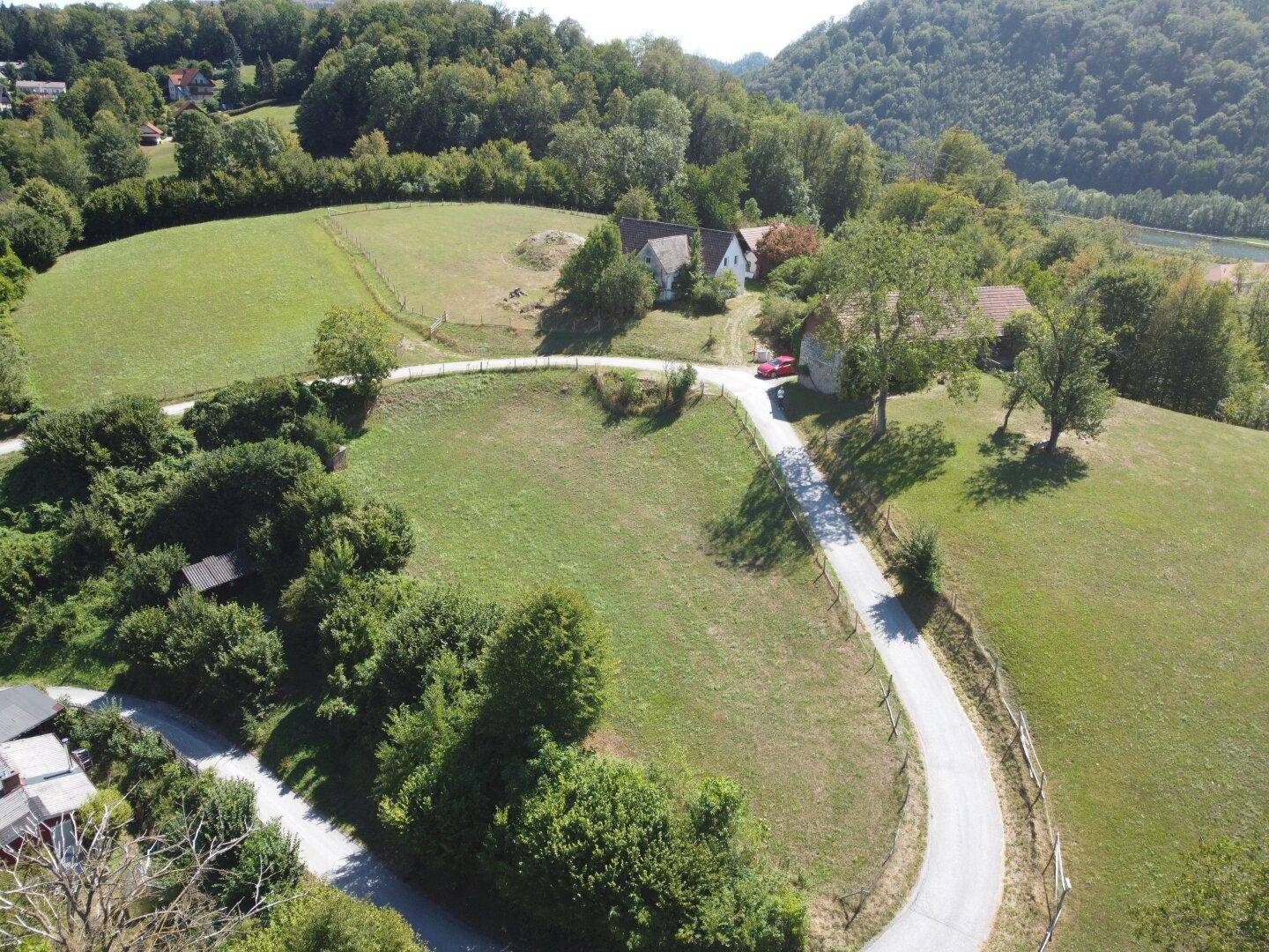 Weitläufige Luftaufnahme einer idyllischen Landschaft mit grünen Hügeln, Feldern und einer kurvigen Straße.