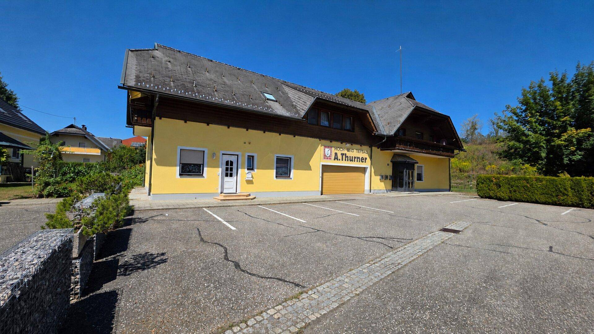 Gelbes Gebäude mit großem Parkplatz und Garagentor unter blauem Himmel.