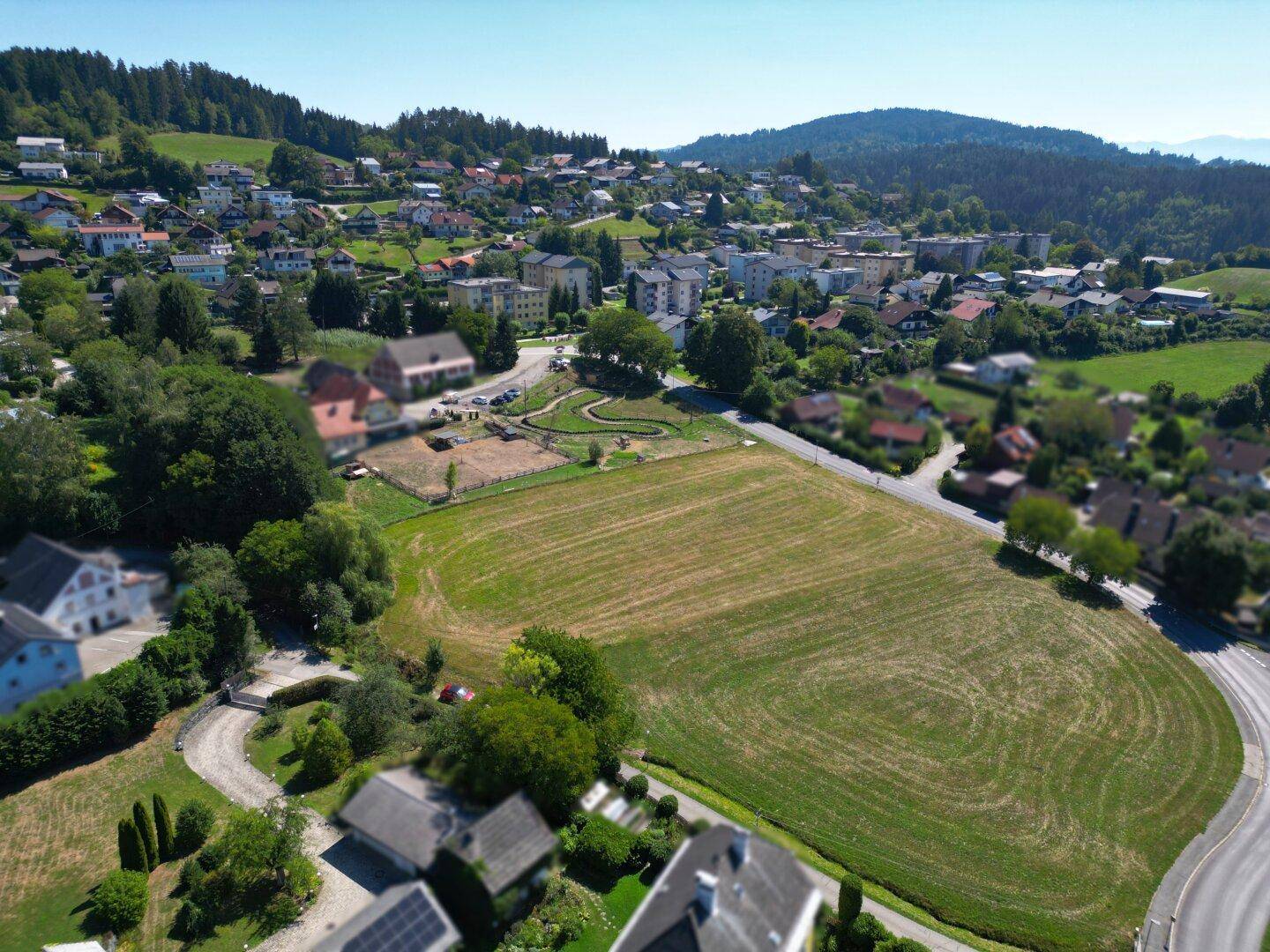 Weitläufiges Grundstück in einer hügeligen Landschaft, umgeben von Wohngebäuden und viel Grün.