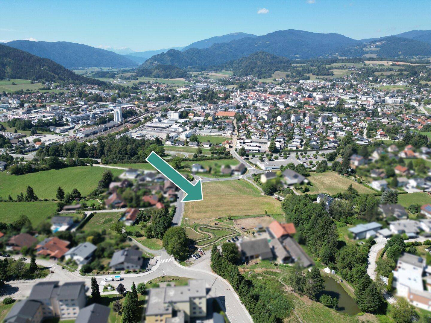 Panoramablick auf eine Siedlung mit einem freien Grundstück, umgeben von Natur und Bergen.